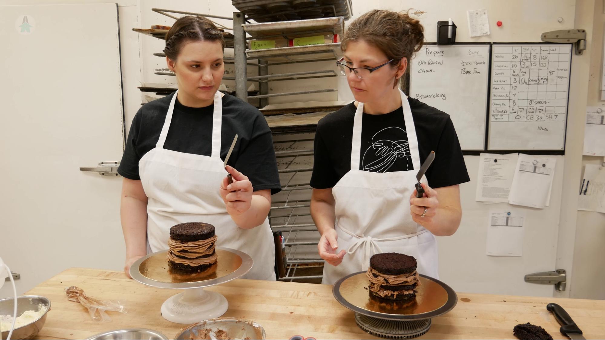 Learning to decorate a cake Cara shows Mel how to hold a cake spatula for icing a cake.